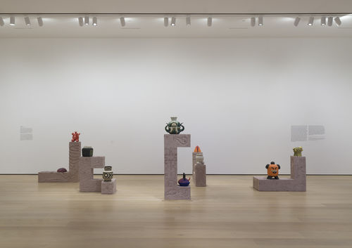 Gallery space with a set of rectangular shaped structures, with colorful ceramic creatures on top of them.