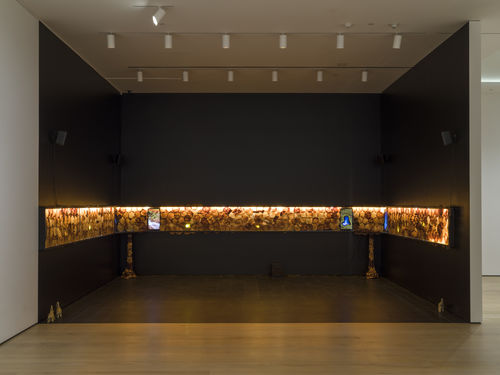 Installation work of hundreds of scobies lined up on the walls of a room, with two screens on each side.