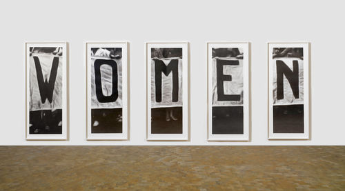 Five large photos of people holding signs that spell out "W-O-M-E-N"