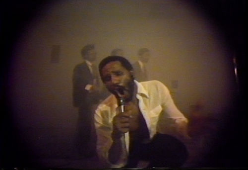 Grainy video still of artist Ulysses Jenkins singing into a microphone