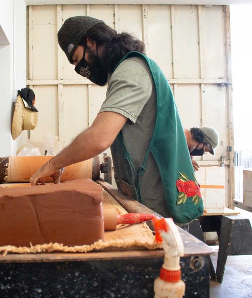 Photo of noé olivas's artist studio, showing two people in masks working over separate tables