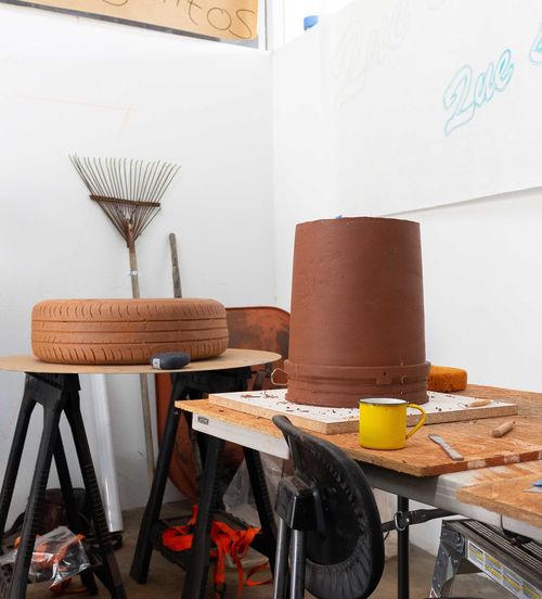 Photo of noé olivas's artist studio, showing sculptures of a tire and an upside down bucket on a worktable