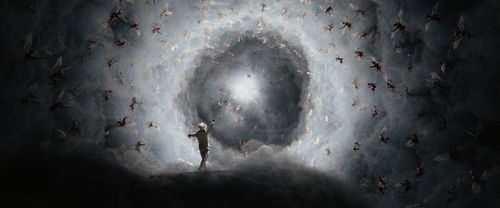 A figure with arms outspread toward a sky full of winged figures circling a bright light