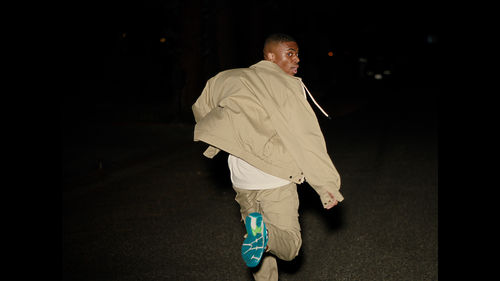 A man in khaki colored pants and jacket running into darkness, looking back toward the camera