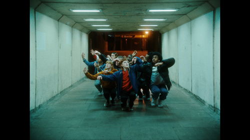 A group of dancers in street clothes crouched and bunched together in a dimly lit tunnel