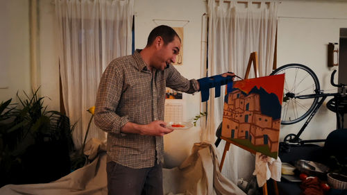 A man talking on a phone, wearing a blue cast and painting a picture of buildings