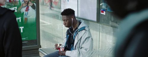A young man sitting on a bench, wearing headphones, and eating a potato chip