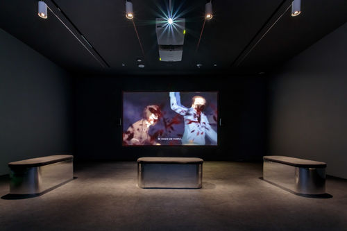 Dark screening room showing video of two anime characters in masks with the caption "Be sincere and truthful."