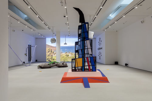 Tall cubist structure and log sculpture in gallery space.