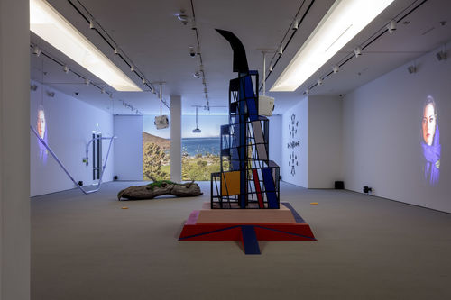 Tall cubist structure and log sculpture in gallery space.