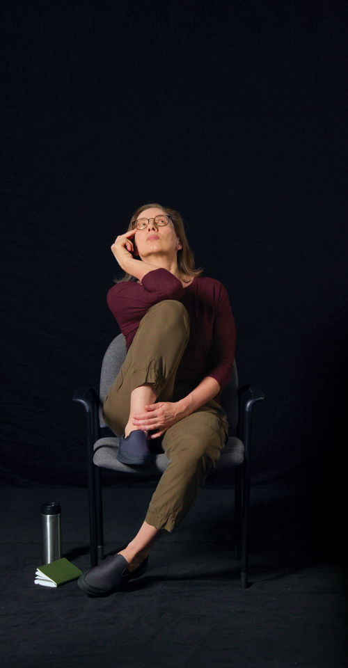 A woman sitting in an office chair holding her right knee up to her chest and her right hand to her face