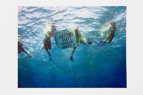 An underwater image looking up at a group of four activists snorkeling, two holding a sign that reads "IT'S GETTING HOT DOWN HERE!!"