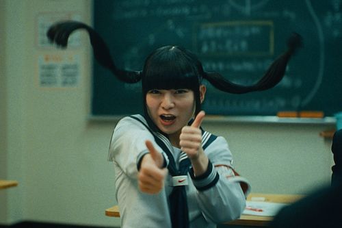 A girl with pigtails in school holds thumbs up.