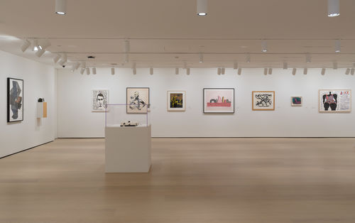Photo of a wide view of a gallery with many framed works on the wall