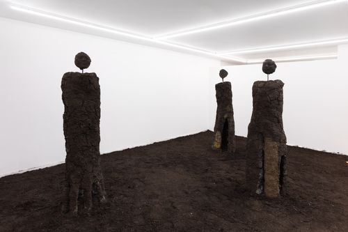 Photo of a gallery with three human-like features, all made of packed earth