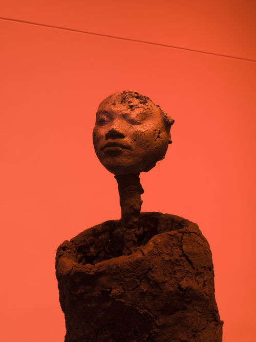  Photo of a sculpture of a form with a human face in an orange-hued room