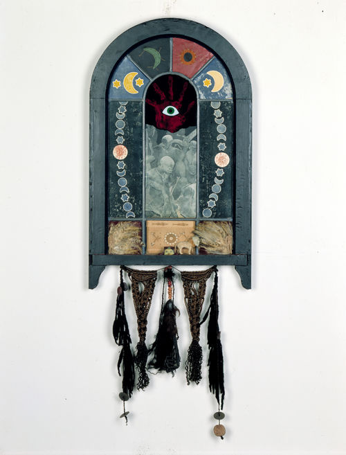 An assemblage of various media in the shape of an arched window, with a single, green eye on a red palm at tits center