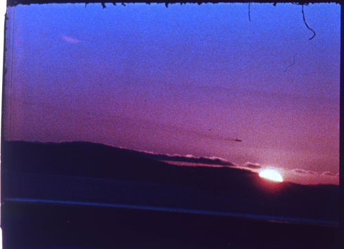 Color film still showing a landscape with the sun setting on the horizon