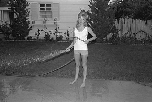 Black and white photo of a woman spraying the sidewalk with a hose
