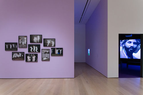 Photo of an exhibition showing a number of framed photographs and a video on a monitor