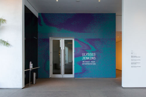 Photo of an exhibition showing the entry wall, featuring the title "Ulysses Jenkins: Without Your Interpretation" over a teal and purple background