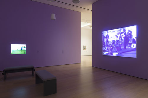 Photograph of a gallery where two videos are projected on lavendar walls