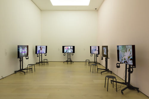 Photo of a gallery where six video monitors line the walls