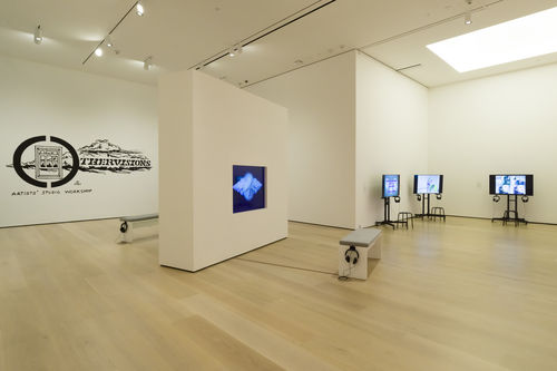 Photo of an exhibition showing a number of video works, as well as the logo for Jenkins' Othervisions Studio