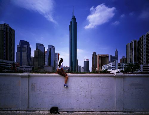 Photograph of a young girl sitting on a wall looking toward the skyline of Shenzhen