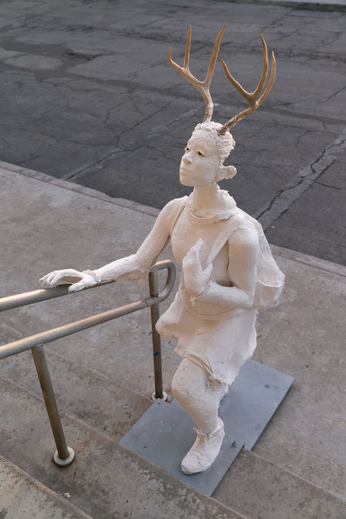 Life-sized plaster figure of a girl with deer antlers, climbing the stairs 