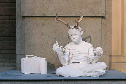 White plaster sculpture of a child with antlers playing cats cradle