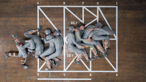 Eight people in identical grey bodysuits lay on the floor, spooning or wrestling with each other