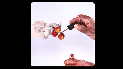 A pair of hands, seen inclose up, paint a bunch of cherries with nail polish