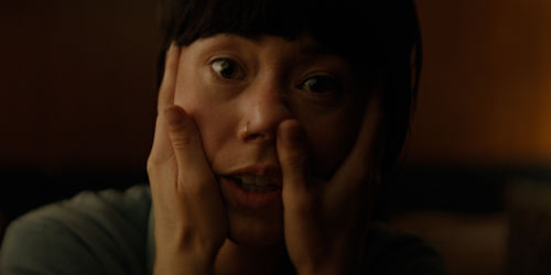 A woman's face seen in close-up, being grabbed by two hands