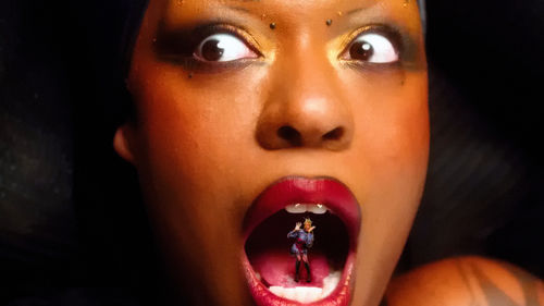 Close up of a Black woman with her mouth open, revealing another person standing on her tongue