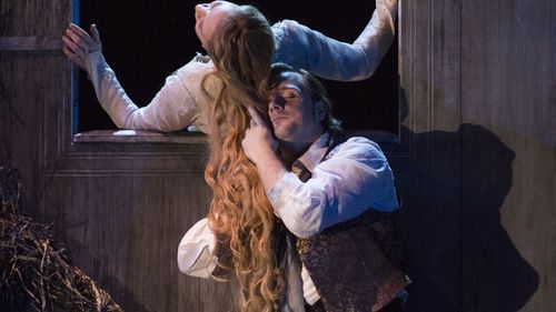 Woman with long hair leans out of window. Man holds her hair.