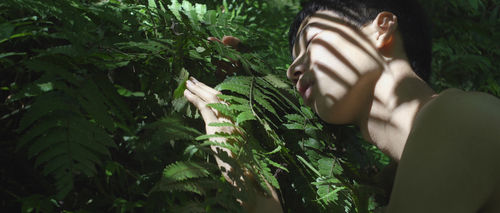 A man rests his face against a fern frond