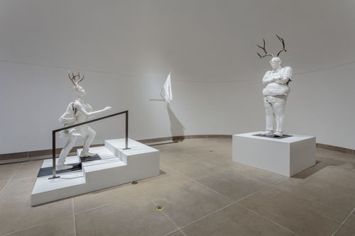 Sculpture of plastered white humanoid walking up stairs and another horned humanoid standing on the right 