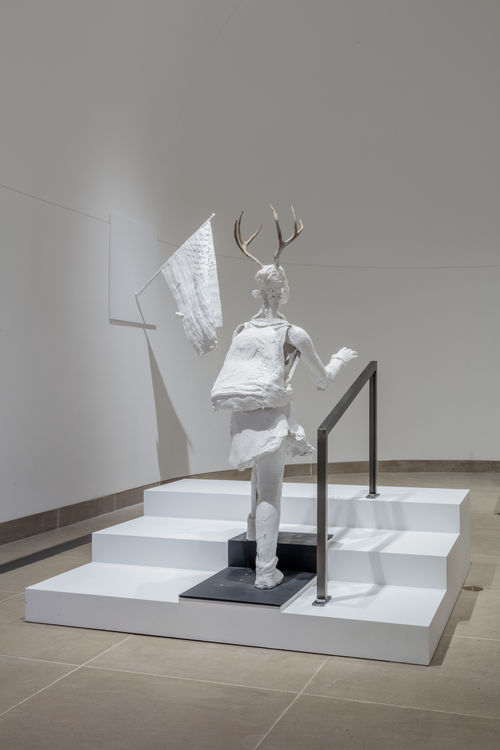 Sculpture of plastered white humanoid walking up stairs