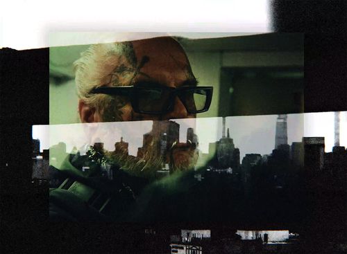 Man with glasses looks through window pane