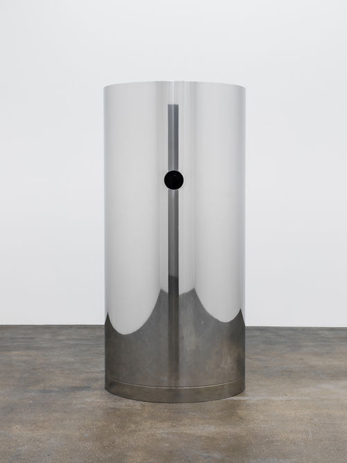 A tall, reflective steel cylinder, with a small hole cut out of it