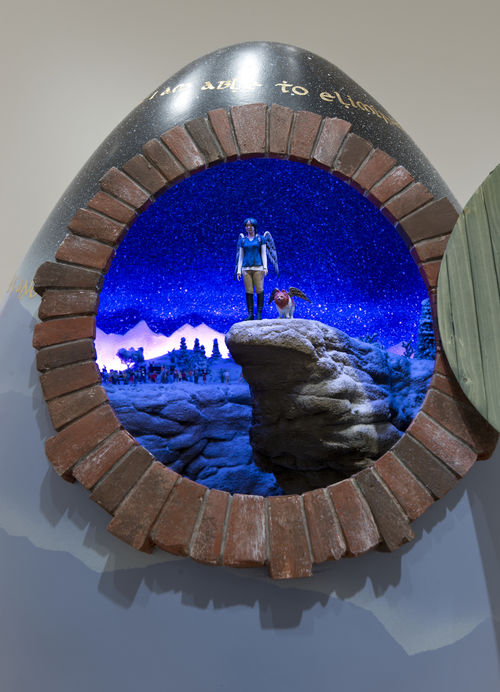 Small-scale sculpture of a woman and a dog ,both with wings on their backs, standing on a rock cliff