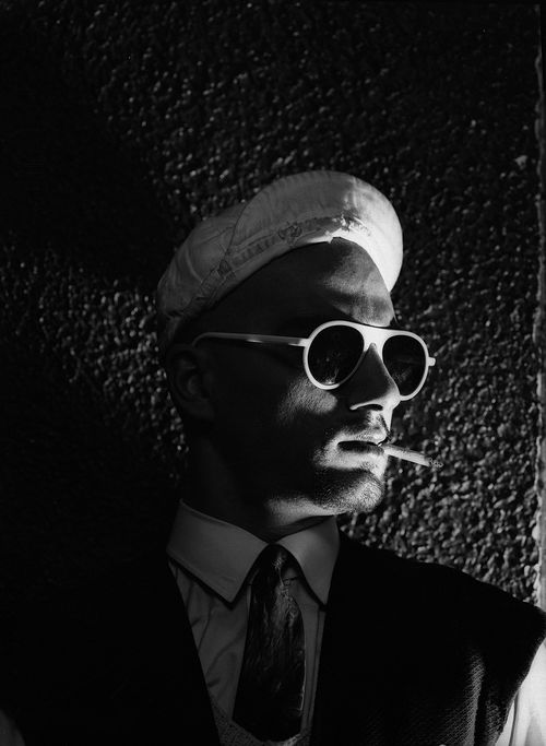 Photo of Van Leo, wearing dark suit, sunglasses, and hat, smoking a cigarette