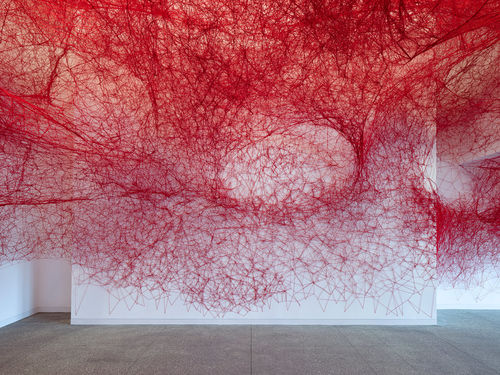Installation view of Chiharu Shiota's installation enveloping the museum lobby in a web of red string