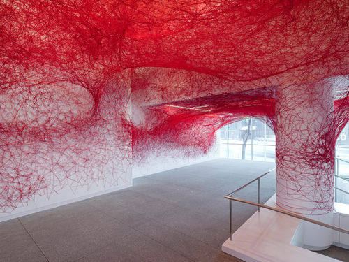 Installation view of Chiharu Shiota's installation enveloping the museum lobby in a web of red string