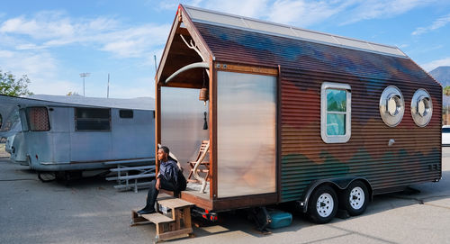 The artist sits on the stoop of a small house on wheels