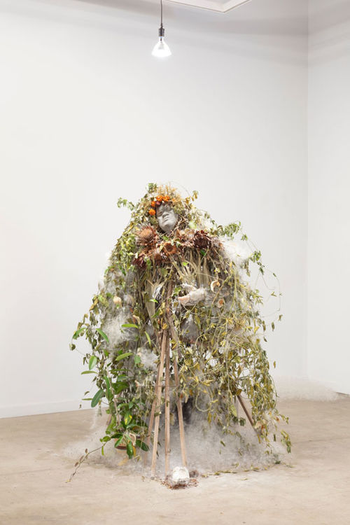 A life-sized figure of a person covered in branches and leaves