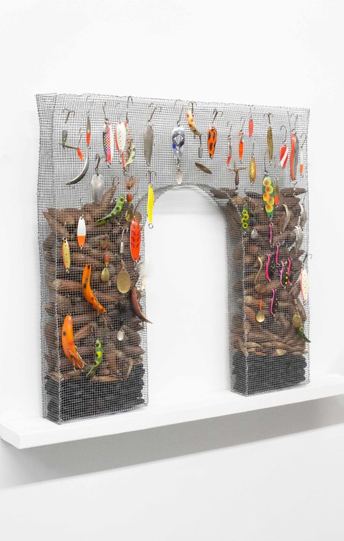 Archway made of chicken wire filled with objects and strewn with fishing lures