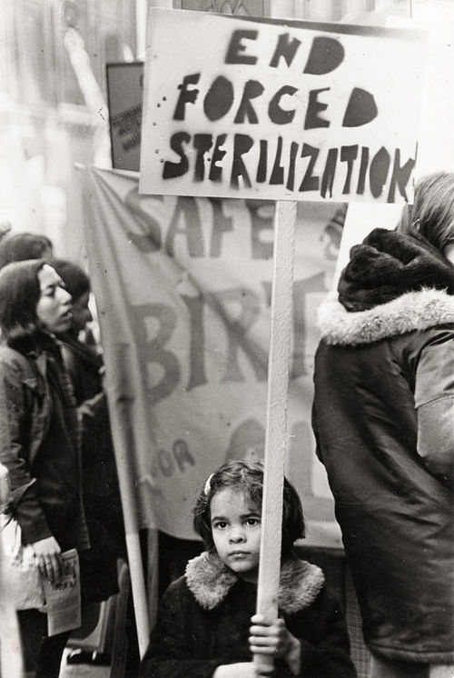 A girl holding a sign reading "End Forced Sterilization"