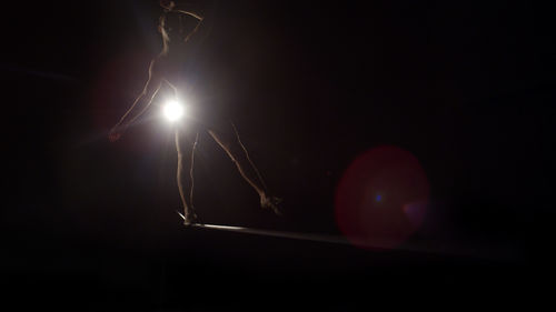 A figure balances on a beam in a dark room
